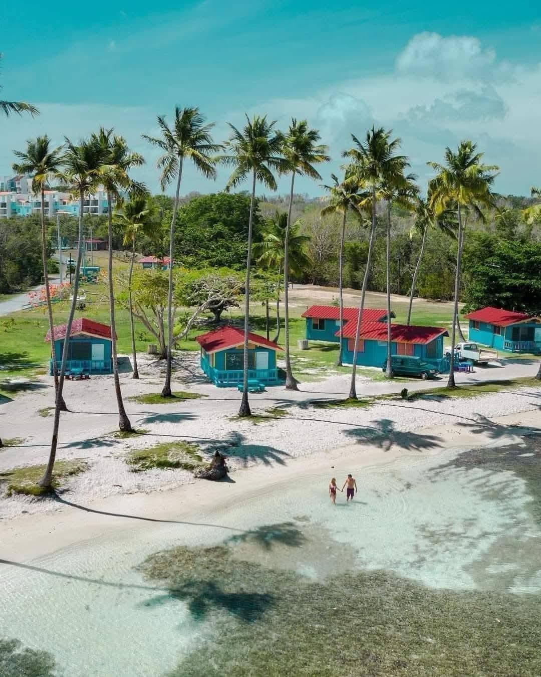 Pareja caminando en el agua cristalina frente a las cabañas
